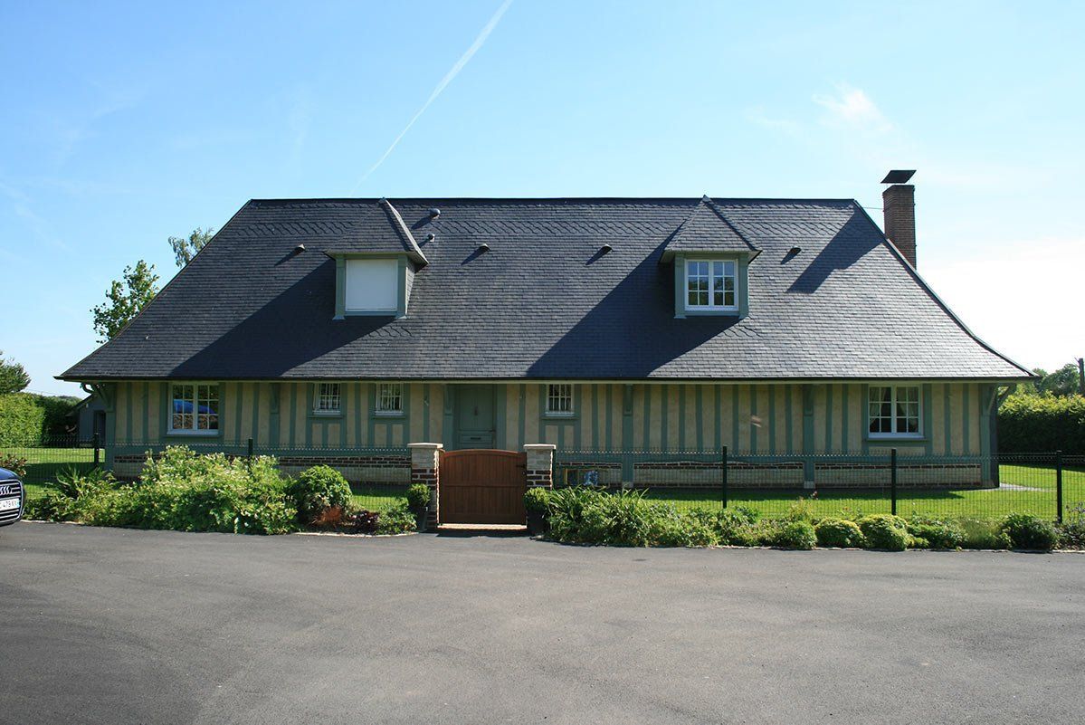 Une maison traditionnelle à colombages avec un toit à pignons sombre, deux lucarnes et un petit portail en bois