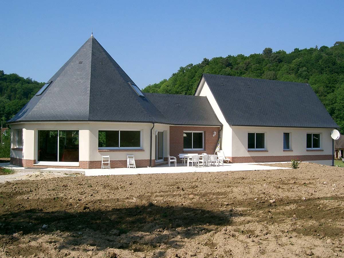 Une maison moderne avec une partie circulaire à toit conique et une aile rectangulaire attenante