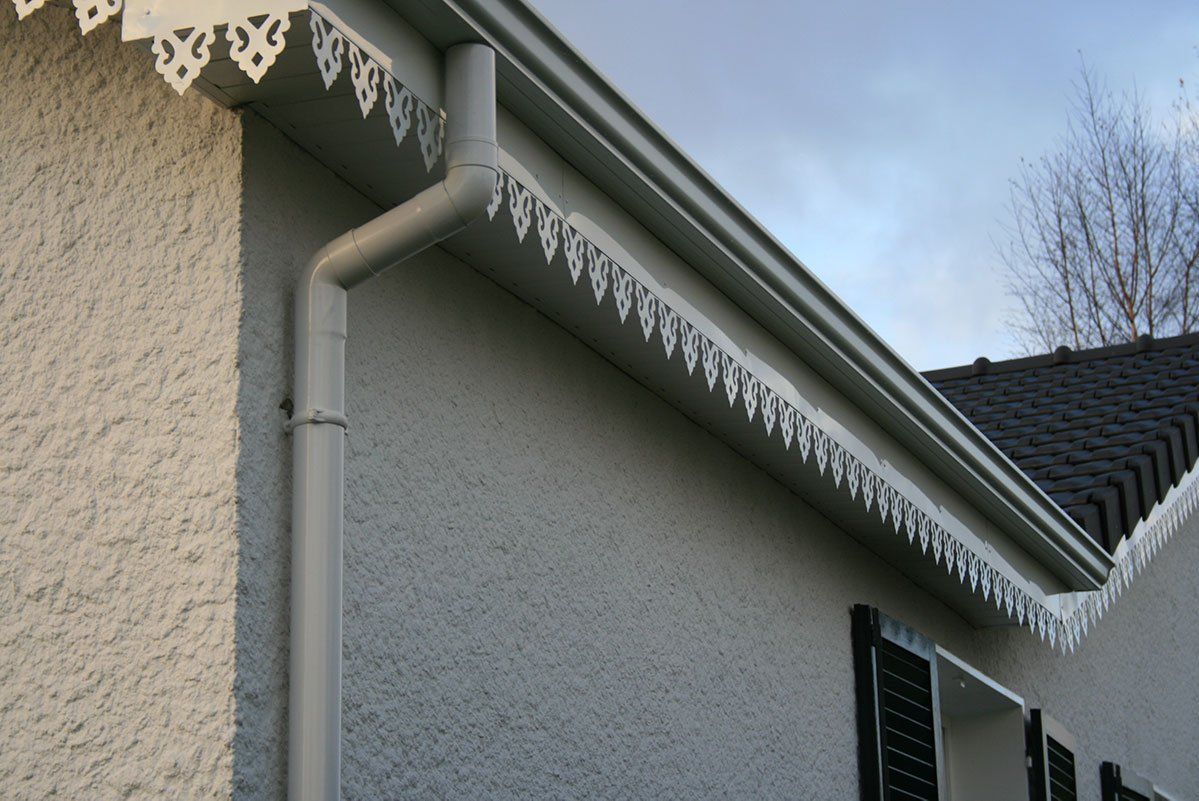 Extérieur de maison blanche avec moulures décoratives, gouttière et descente pluviale.
