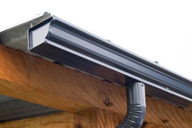Gouttière gris foncé fixée à une structure en bois, avec une descente pluviale.