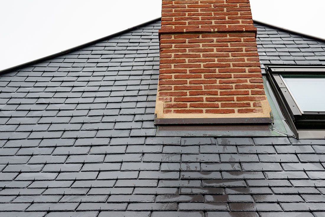 Une cheminée en briques s'élève d'un toit de bardeaux de couleur sombre, percé d'une lucarne sur le côté droit.
