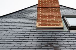 Une cheminée en briques s'élève d'un toit de bardeaux de couleur sombre, percé d'une lucarne sur le côté droit.