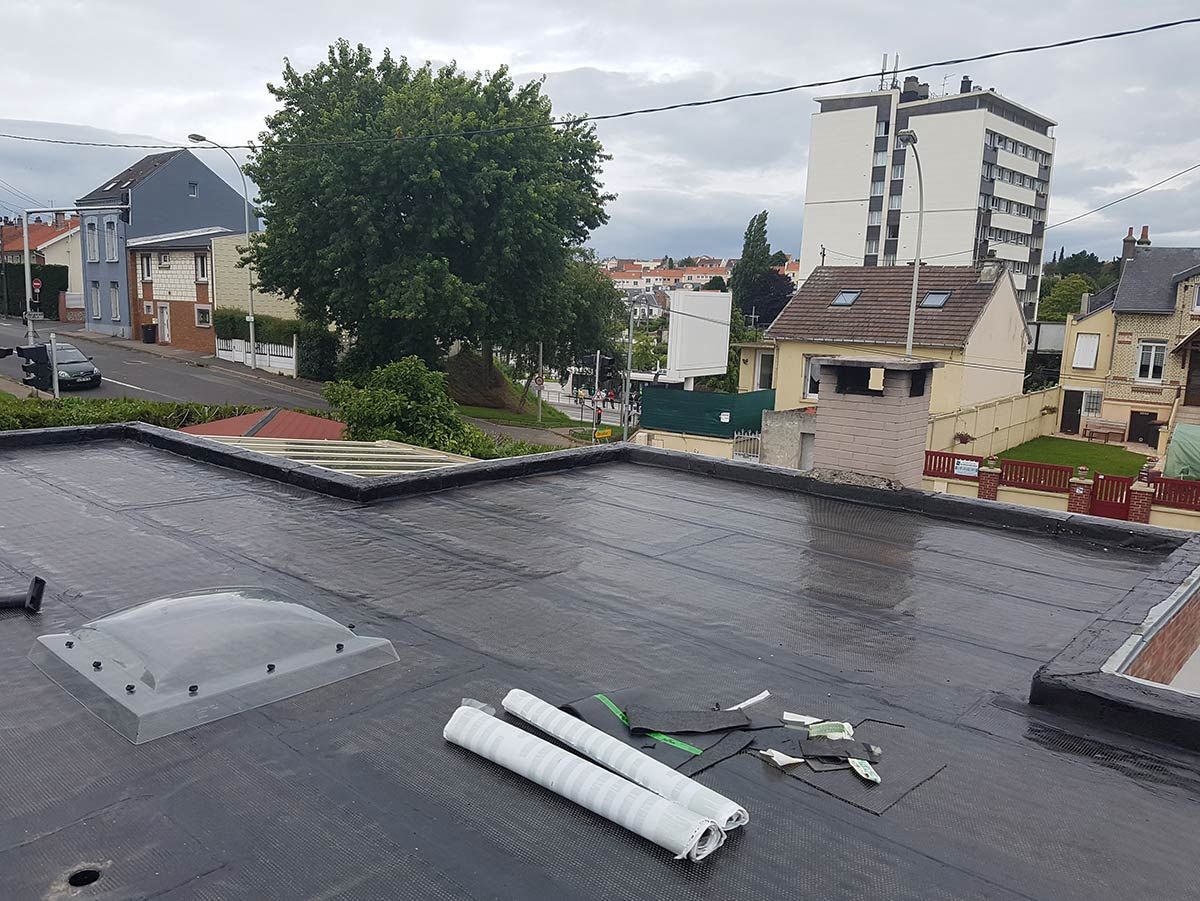 Toit plat noir avec vue urbaine ; arbre, bâtiments, ciel nuageux, matériaux de construction.