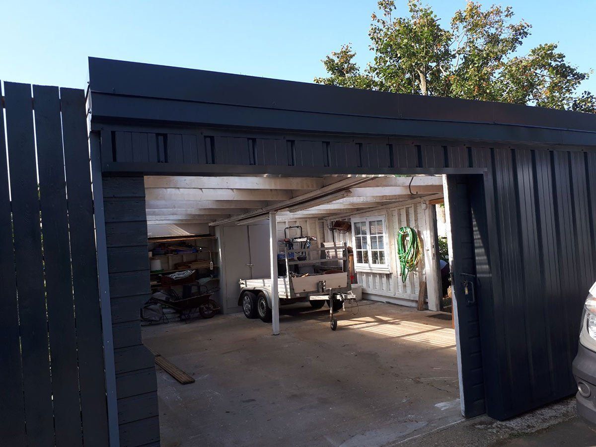 Un hangar gris foncé aux portes ouvertes ; une petite remorque est garée à l'intérieur.