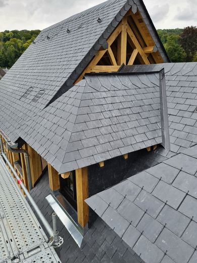 Un toit en ardoise avec des poutres en bois apparentes, un angle de bâtiment et un échafaudage.