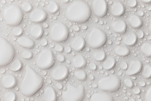 Des gouttelettes blanches et brillantes, de tailles variables, sont dispersées sur une surface blanche.