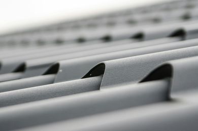 Gros plan sur un toit en tôle ondulée grise aux nervures incurvées et sur un fond flou.