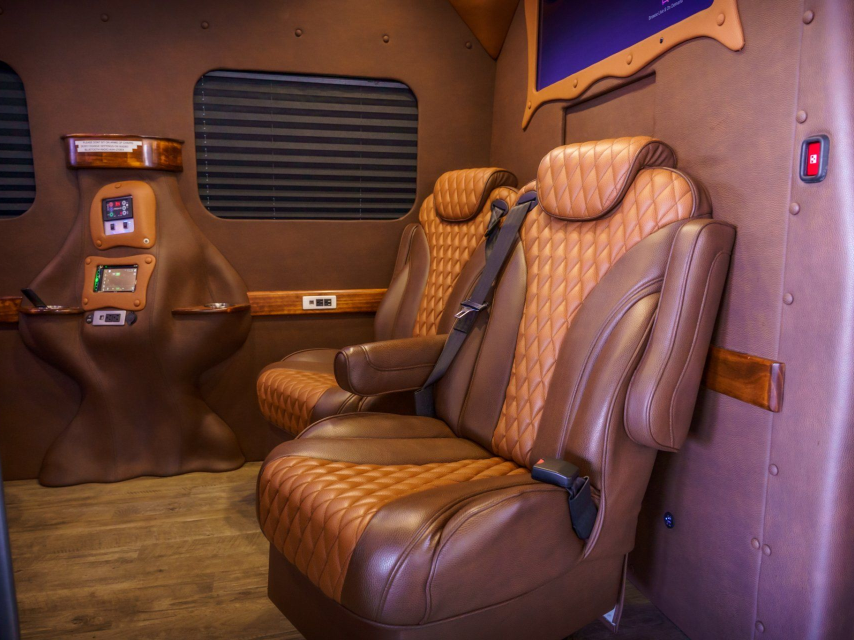 Brown leather interior of a vehicle with two captain's chairs, a control panel, and a window.