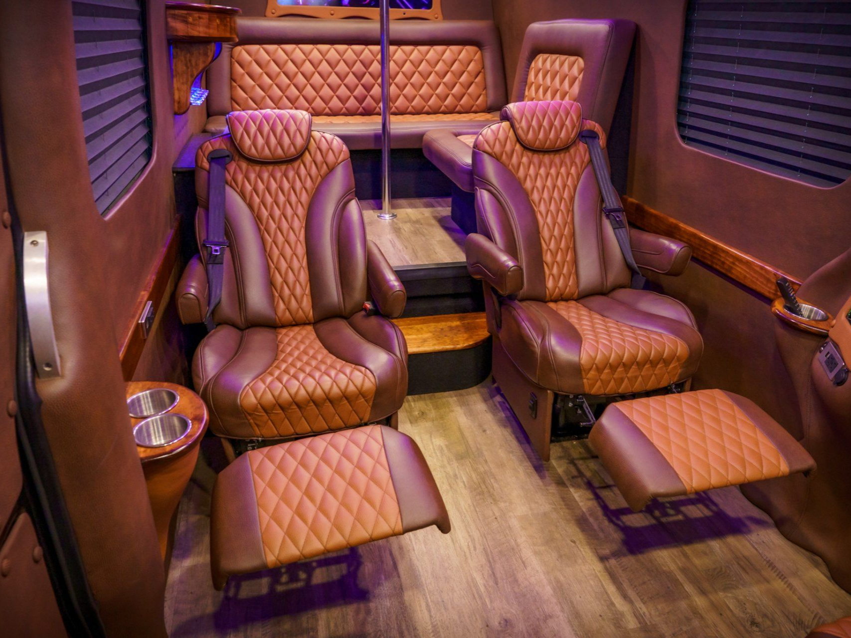 Luxurious van interior with brown leather seating, footrests, and wood flooring.