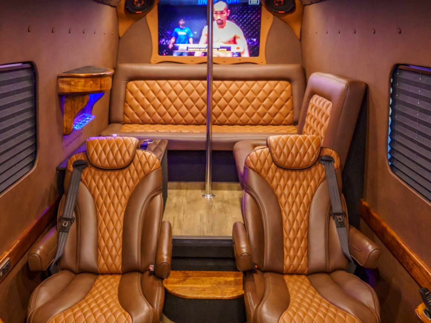 Luxury van interior with brown leather seating, a pole, and a TV screen displaying a video.