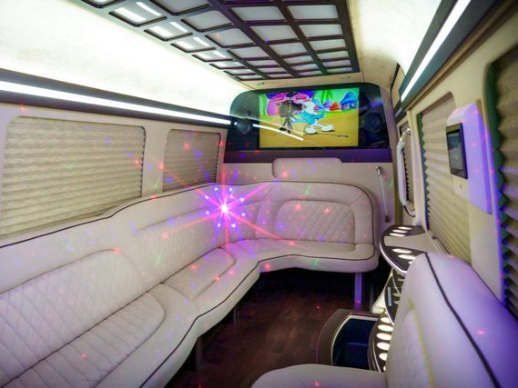 Interior of a white limousine with leather seating, a TV playing a cartoon, and laser lights.