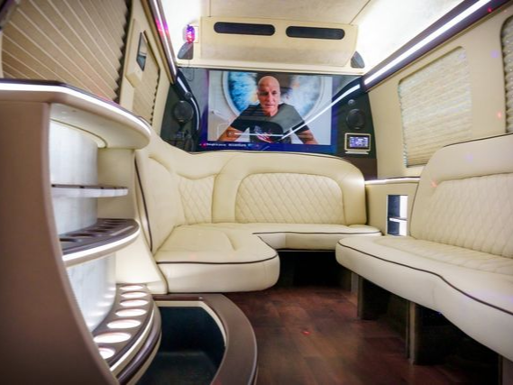 Luxurious van interior with cream leather seats, television screen, and wood flooring.