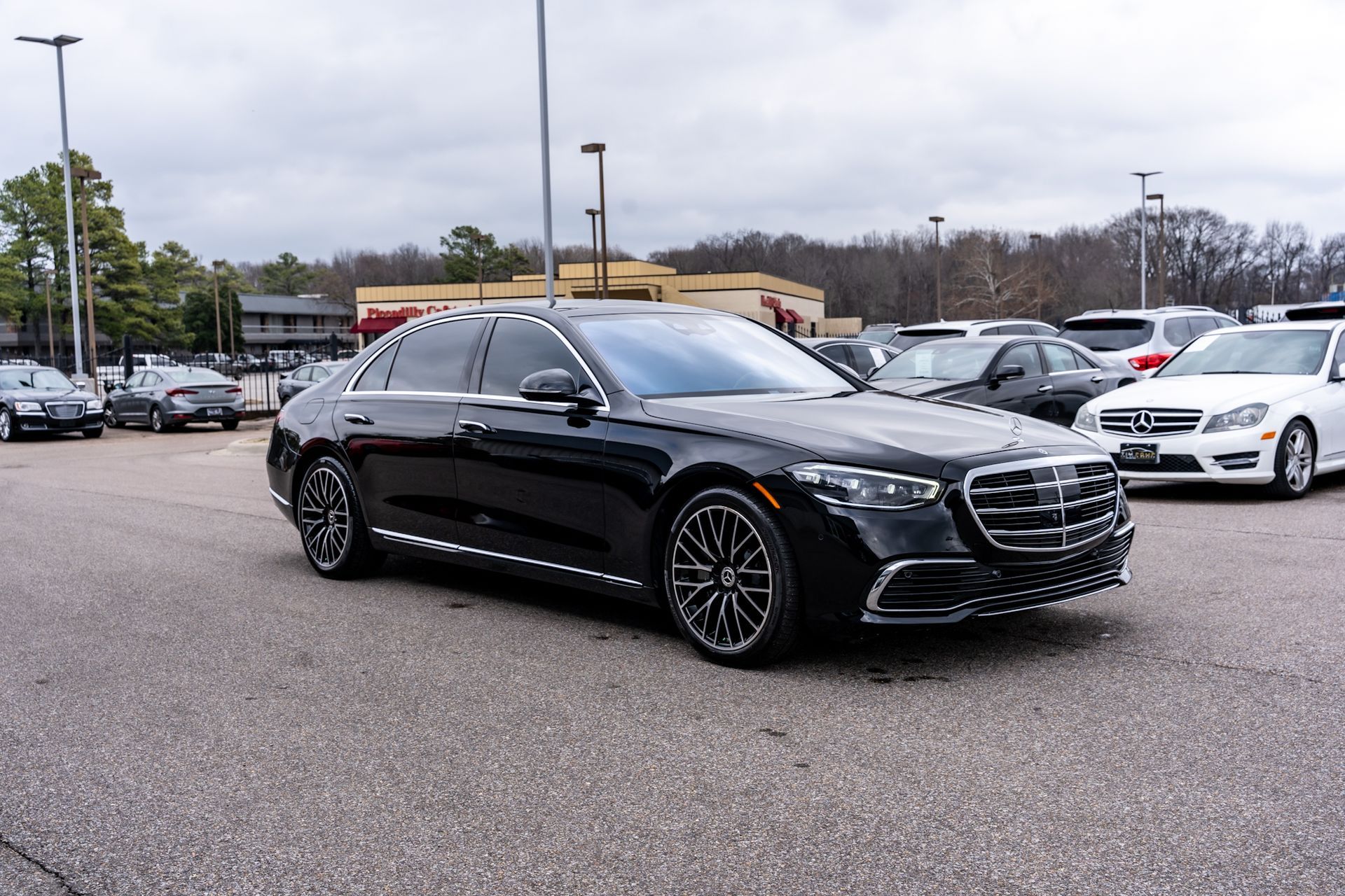 Black Mercedes sedan parked in a lot; other cars and buildings are in the background.