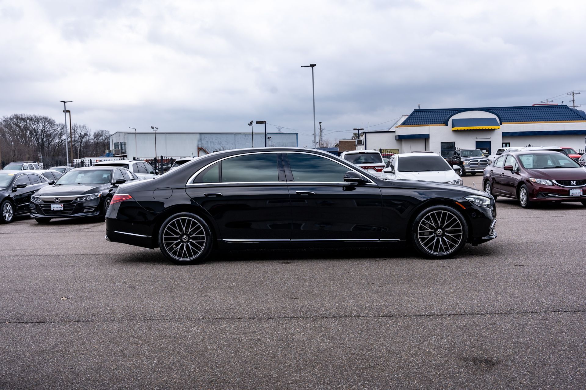 Black sedan with custom wheels parked in a parking lot. Cloudy sky overhead. Other cars visible.
