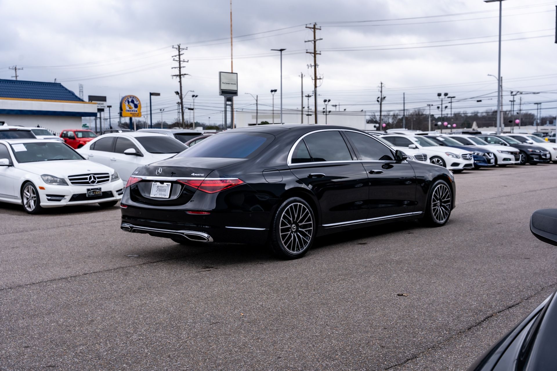 Black Mercedes sedan on a car lot, surrounded by other vehicles on an overcast day.