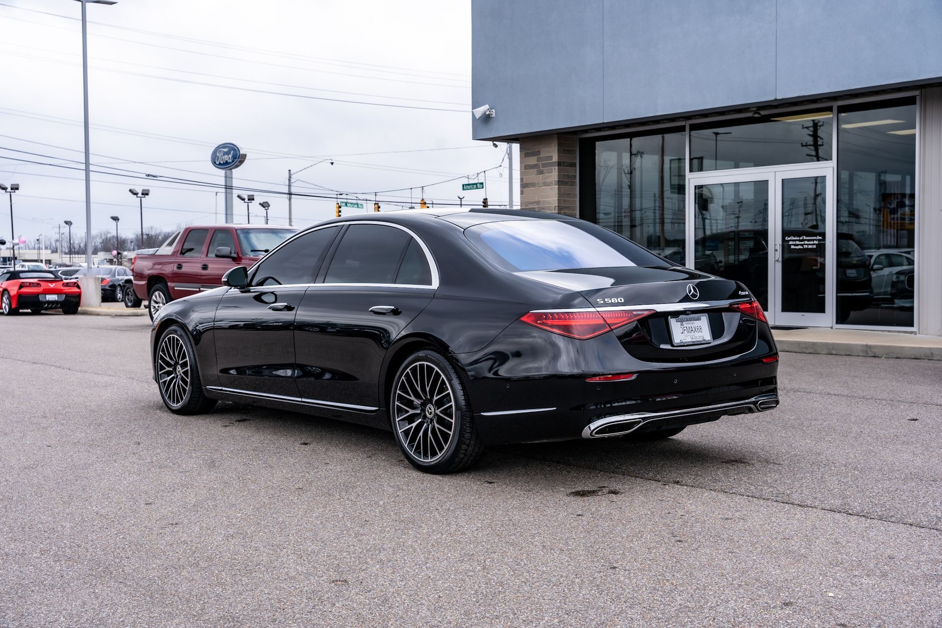 Black Mercedes-Benz sedan parked on asphalt outside a car dealership.