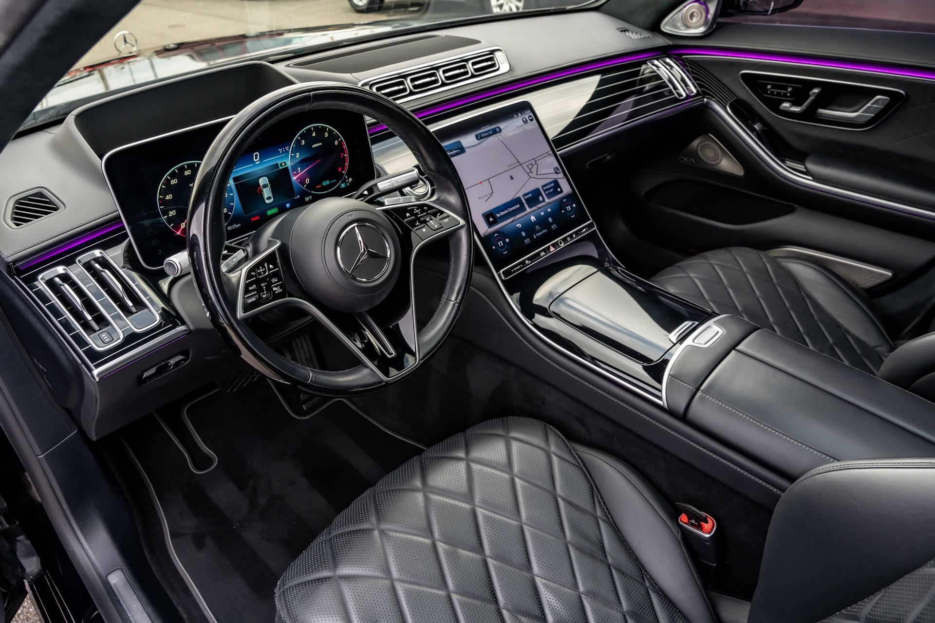 Interior view of a Mercedes-Benz luxury car, black leather seats, large touchscreen display, ambient purple lighting.