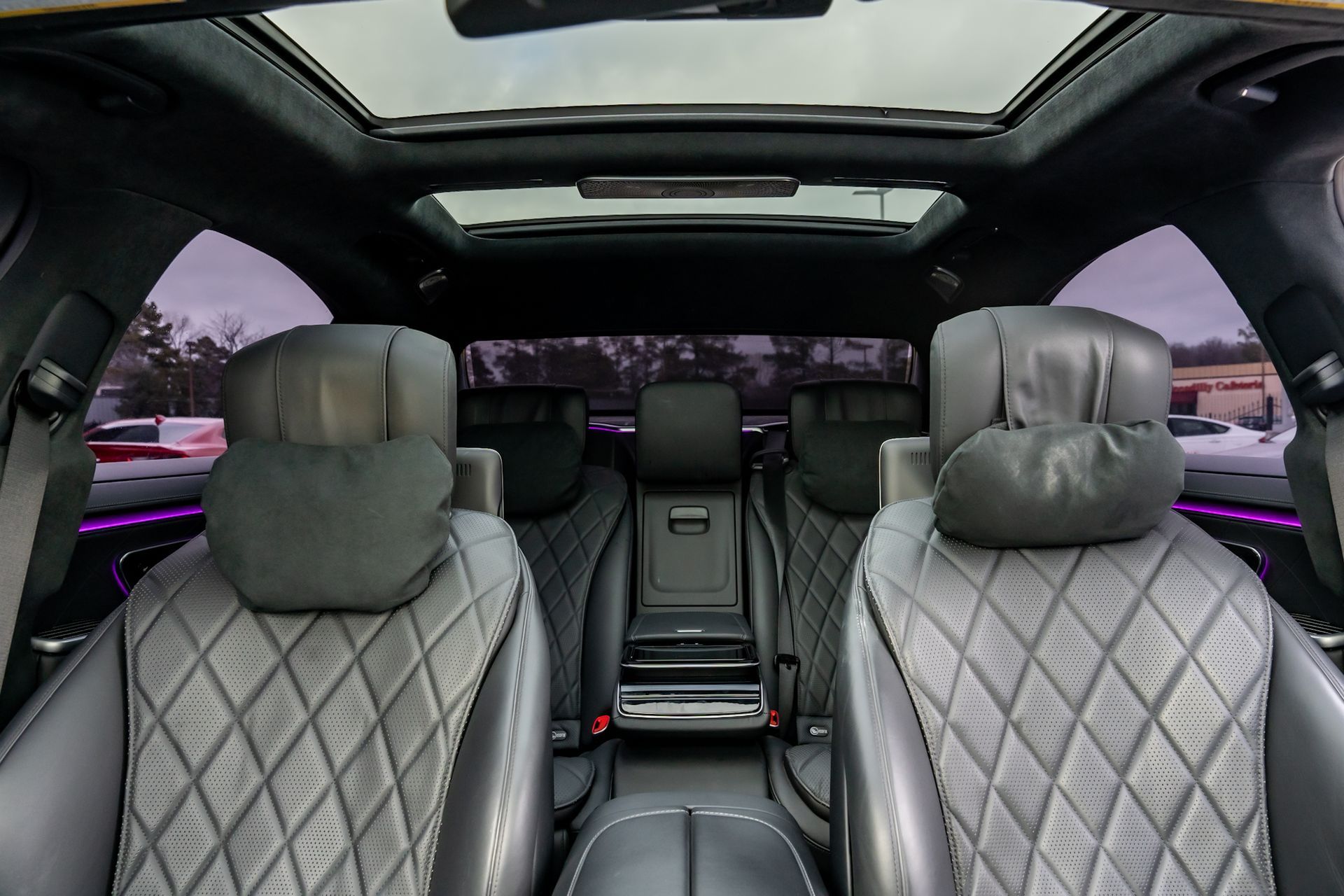Interior view of a luxury car with black leather seats, a panoramic sunroof, and ambient lighting.