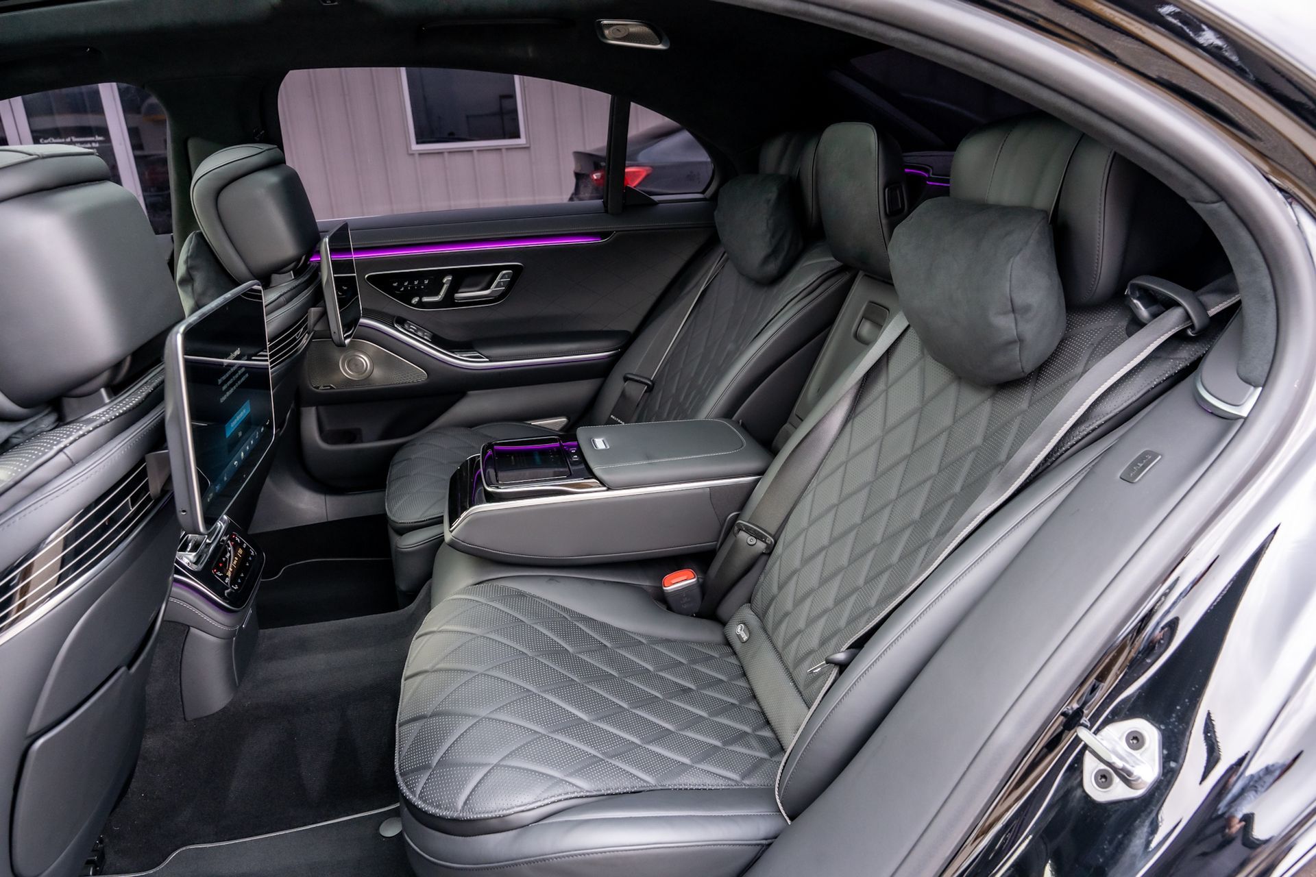 Black luxury car interior with quilted leather seats, armrest, and digital screens.
