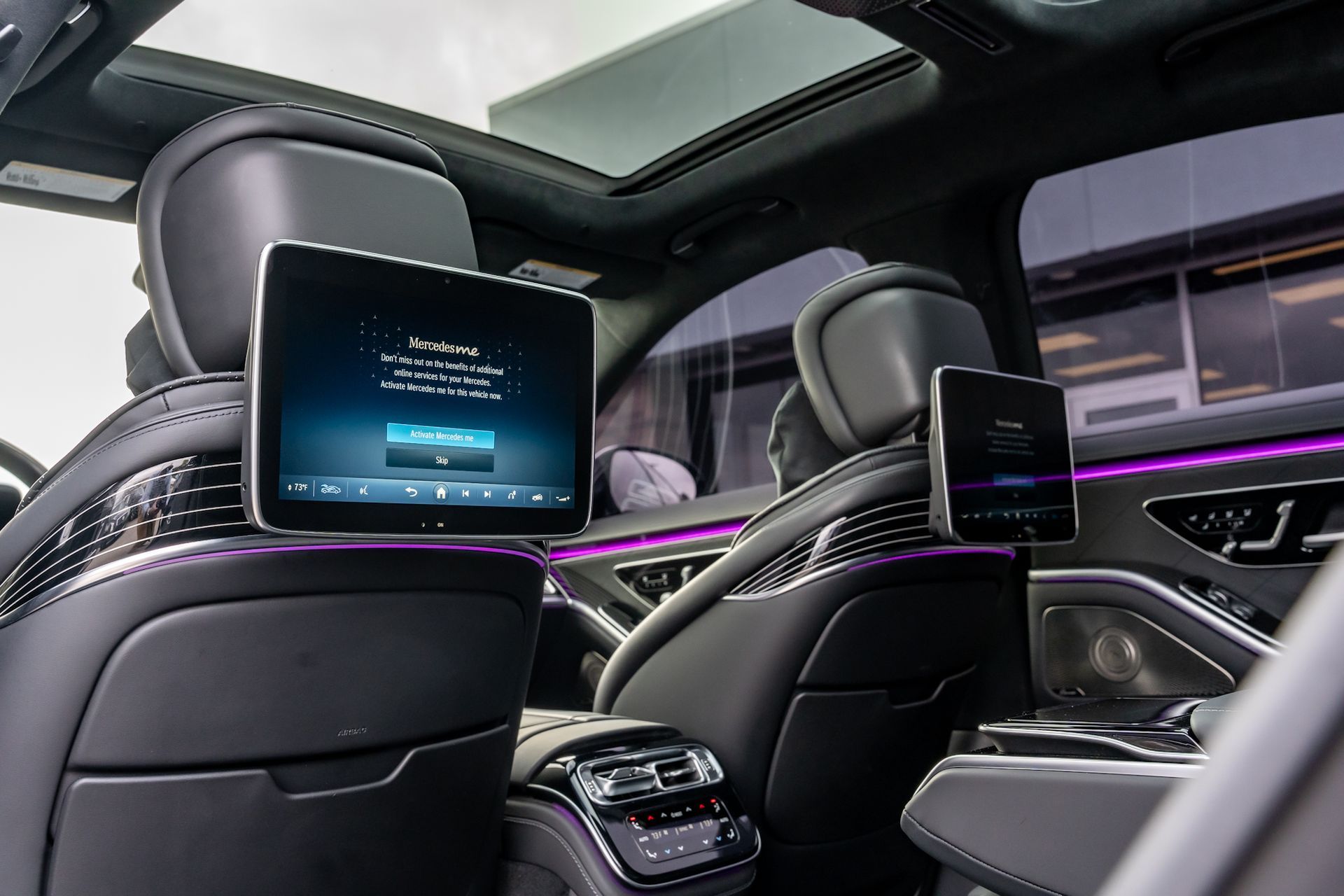 Backseat of a luxury car with two screens, dark interior, ambient purple lighting.