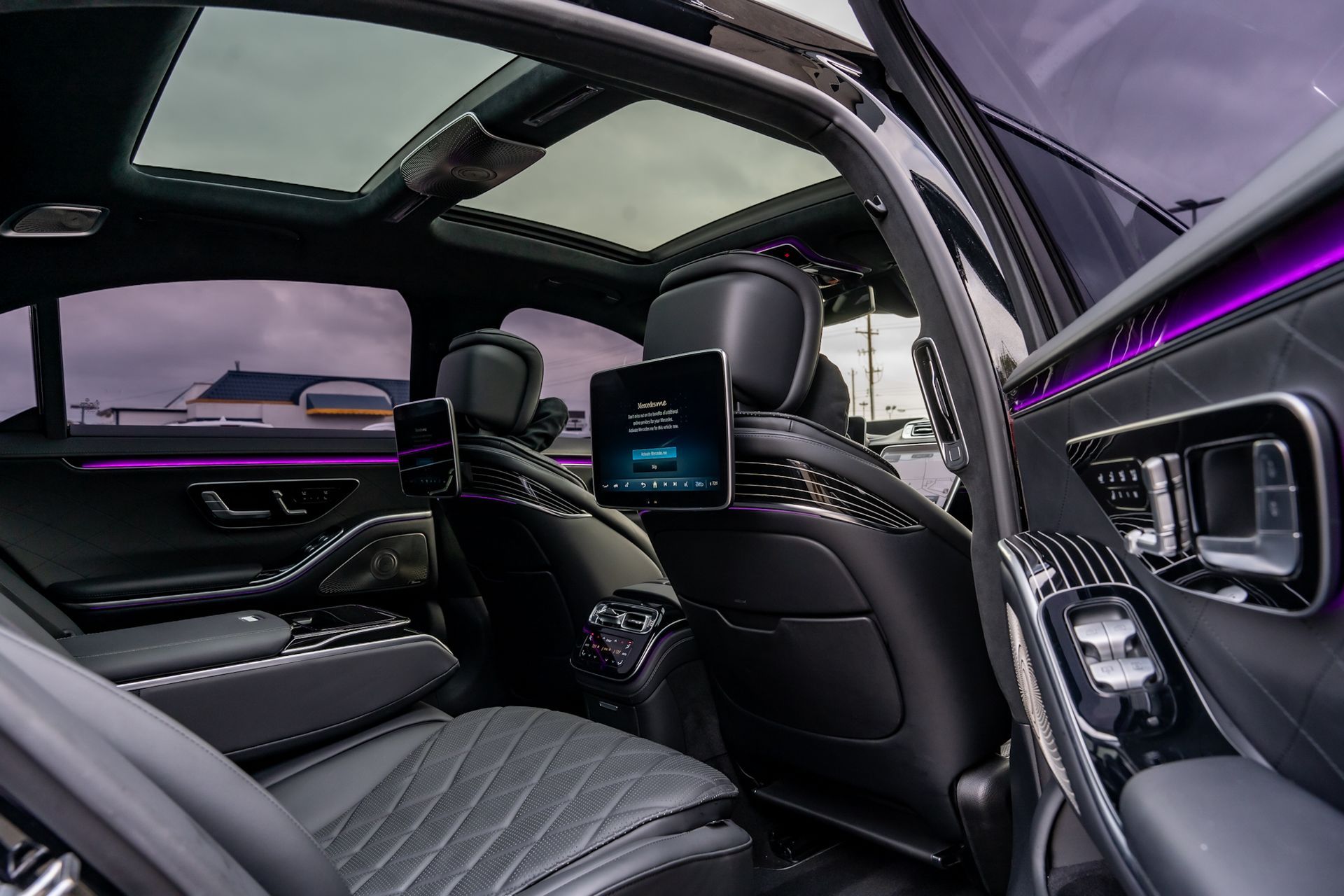 Luxurious car interior: black leather seats, built-in screens, purple ambient lighting, and a panoramic sunroof.
