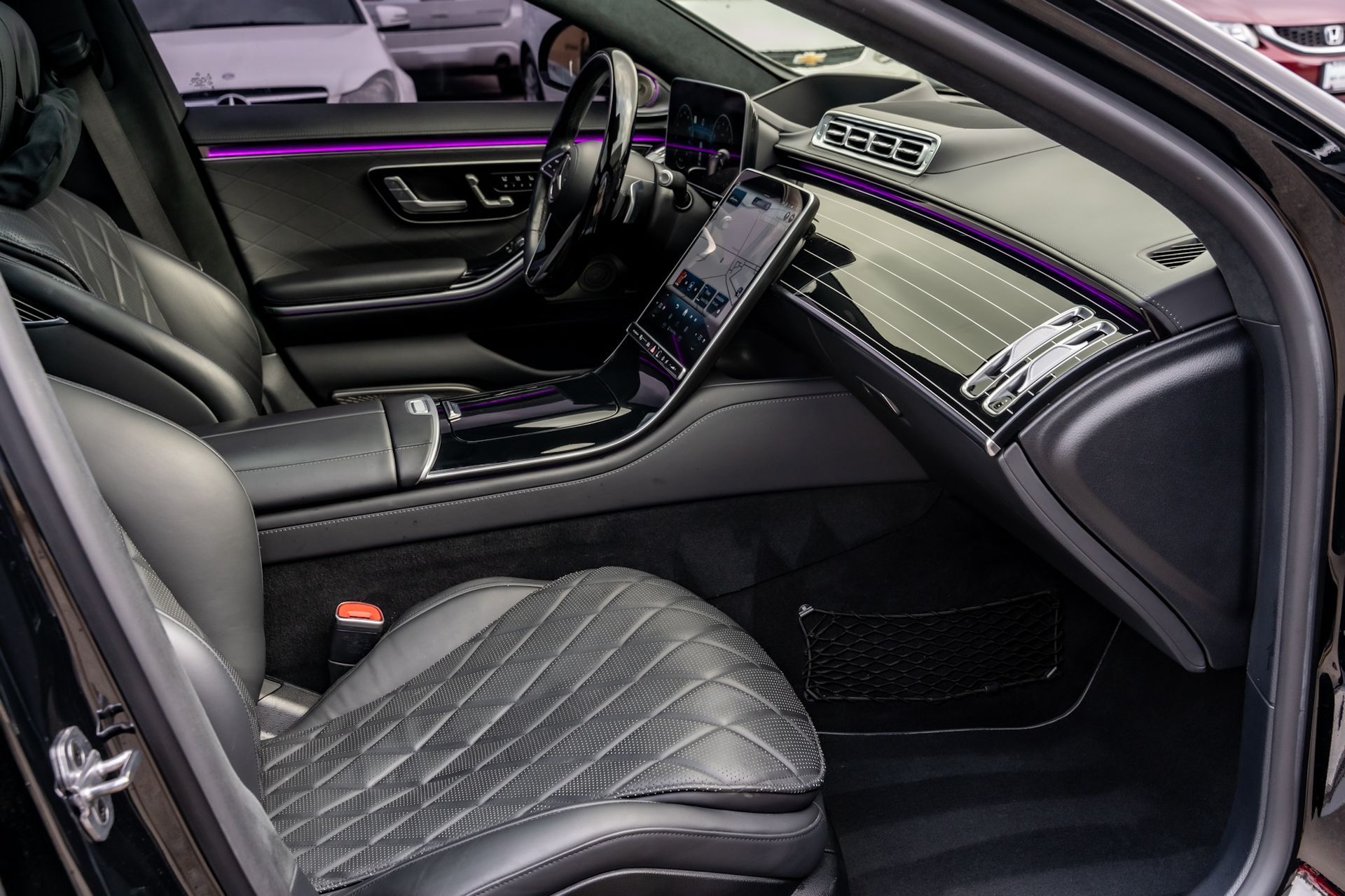 Black Mercedes-Benz interior with leather seats, dashboard, and touchscreen display. Purple ambient lighting.