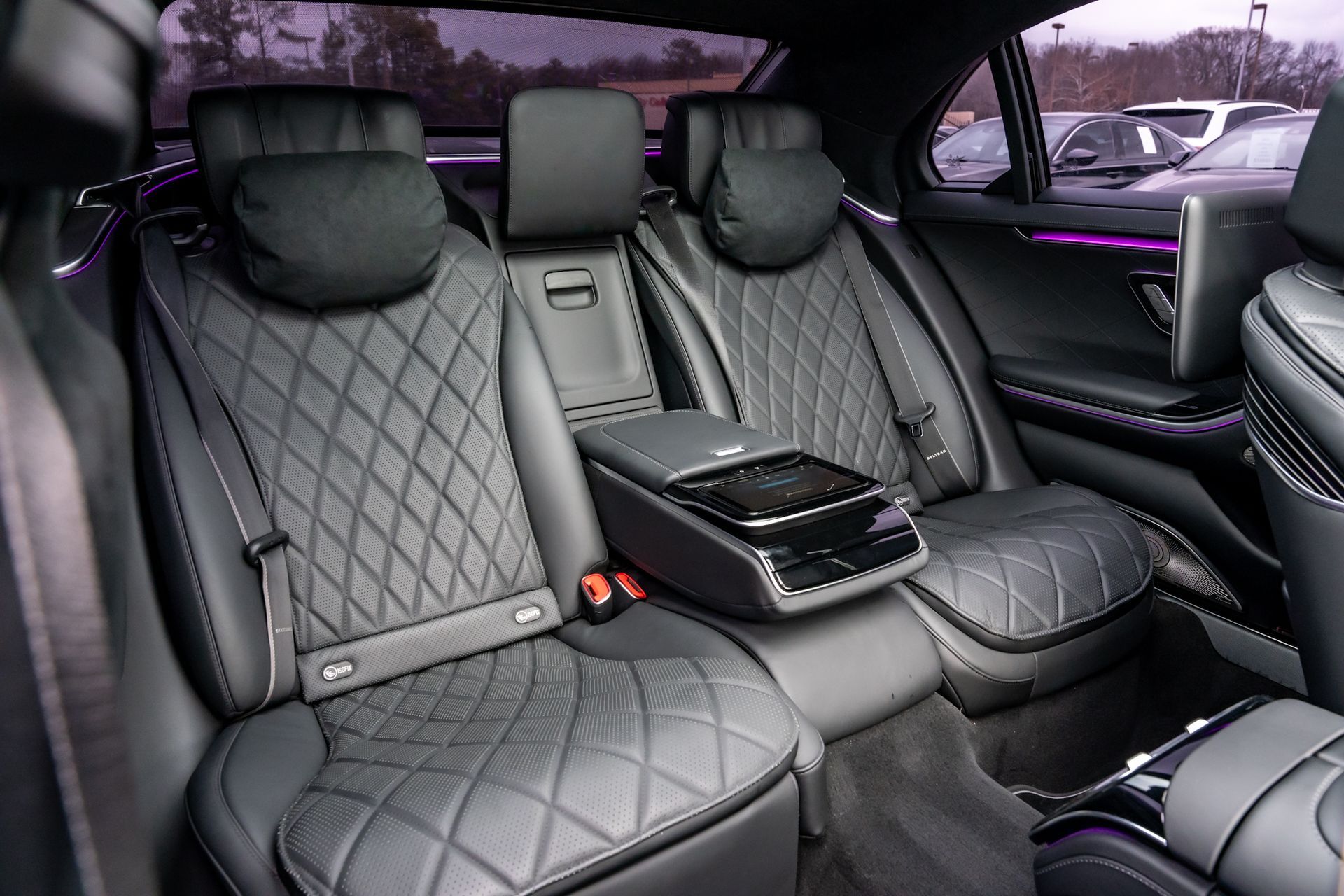 Back seat of a luxury car with black diamond-stitched leather upholstery, armrest, and headrests.