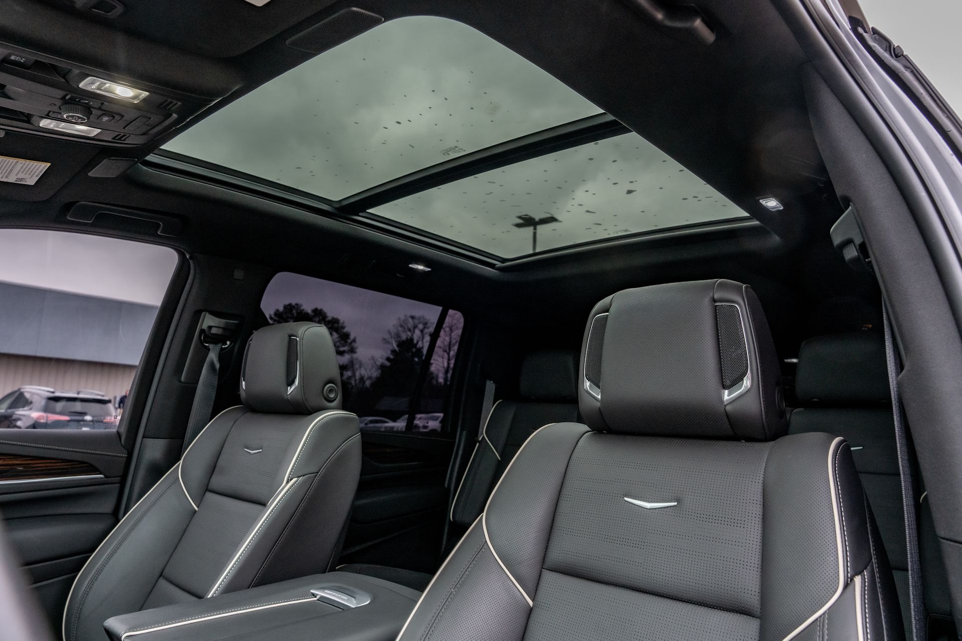 Interior of a black SUV with a panoramic sunroof, showing leather seats with white stitching.