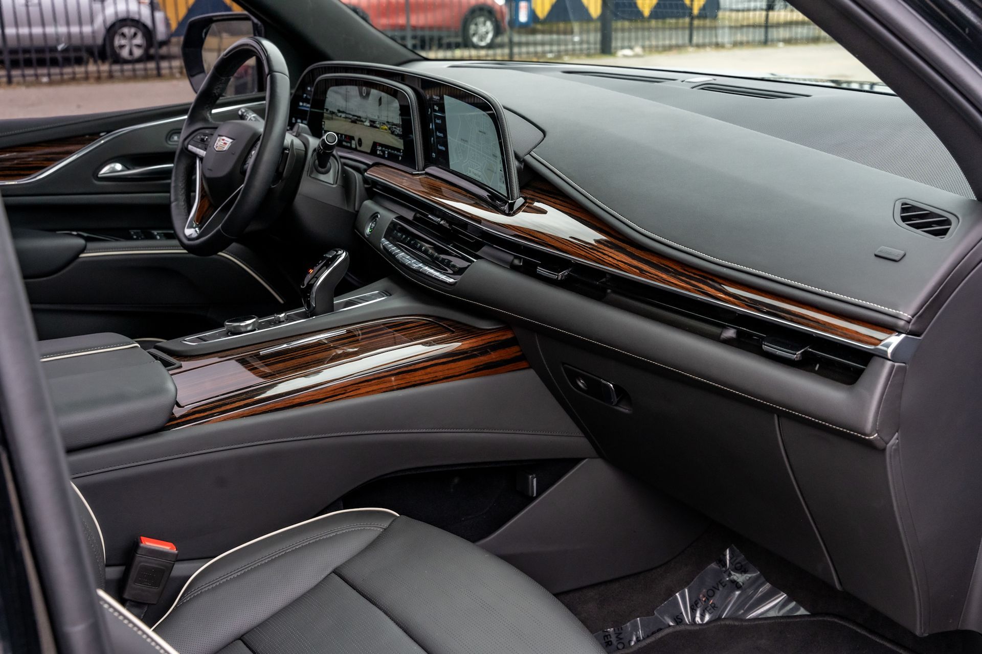 Interior view of a black Cadillac Escalade; dark wood accents, leather seats, digital display, and steering wheel.