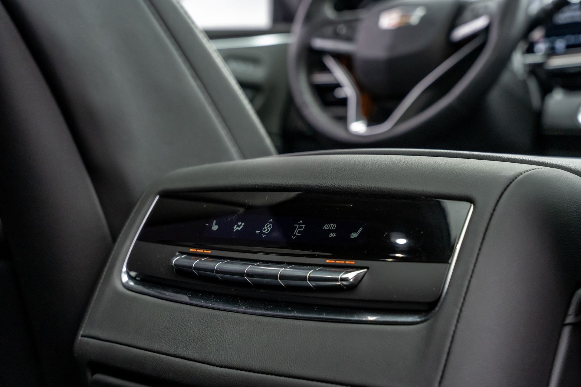 Black leather car console with climate control buttons, steering wheel in background.