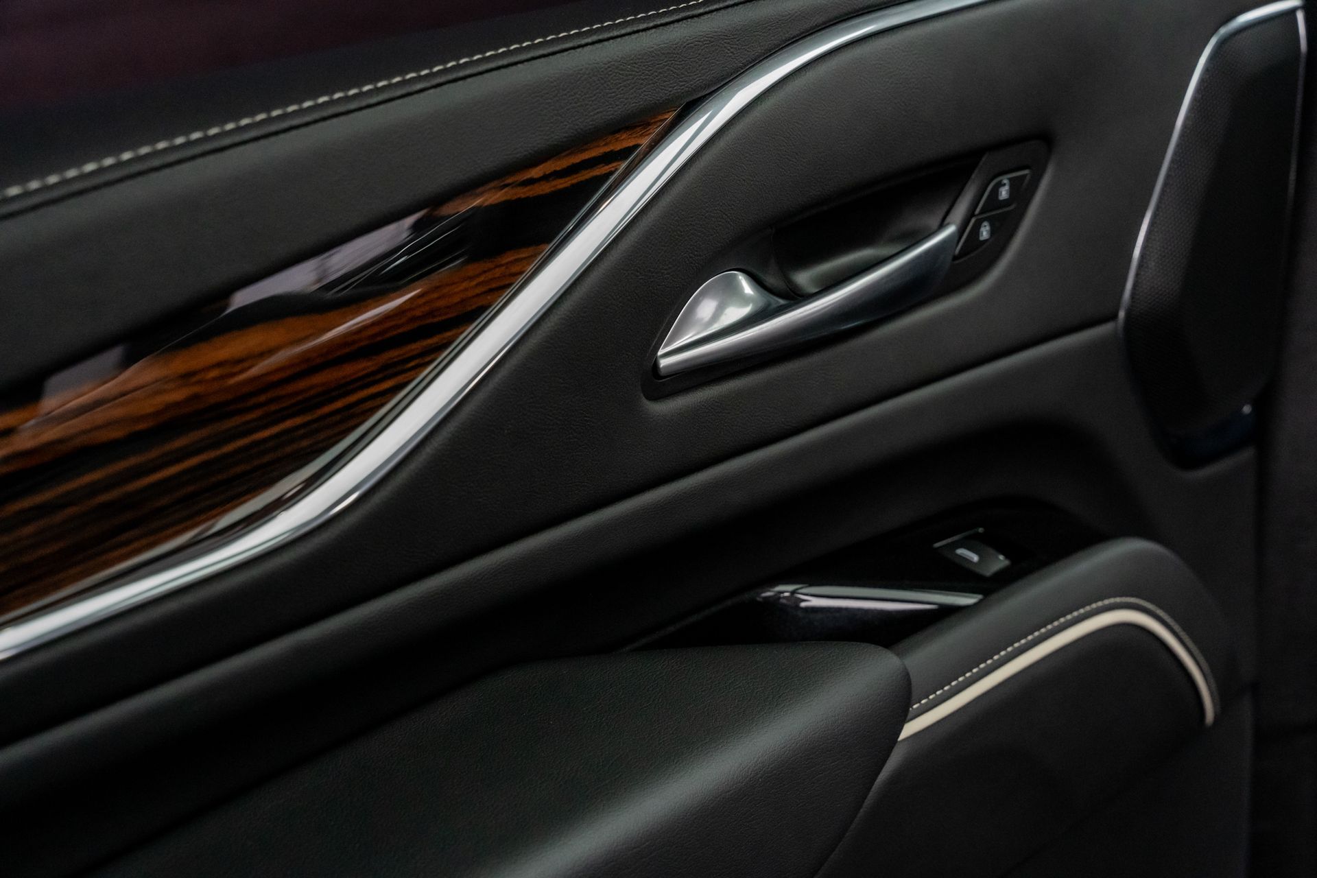 Close-up of a luxury car door interior; black leather, wood grain trim, chrome accents, and door handle.