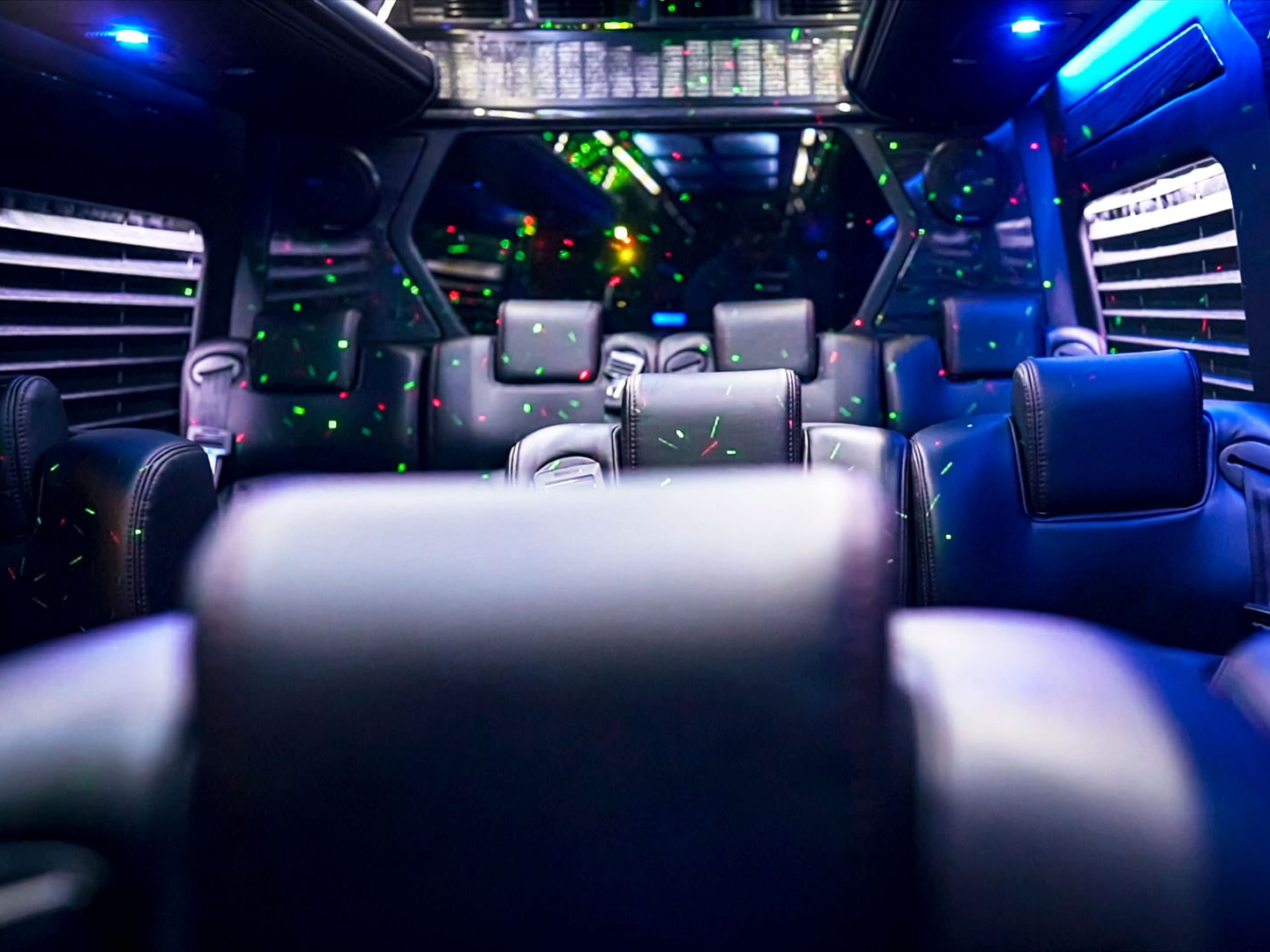 Interior of a party bus with black leather seats, disco lights, and a window with blinds.