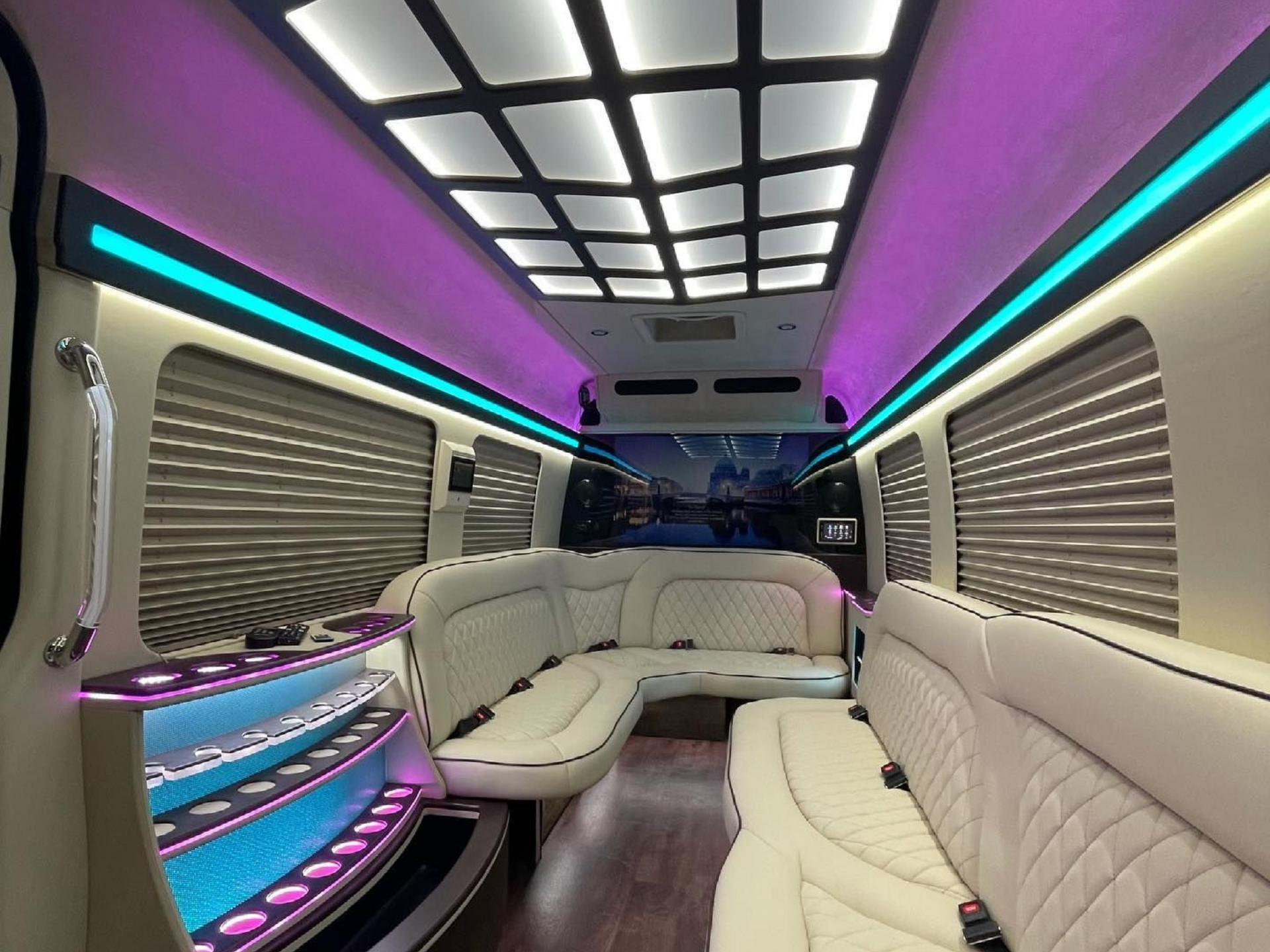 Interior of a luxury van with cream leather seating, colorful lighting, and a cityscape mural.