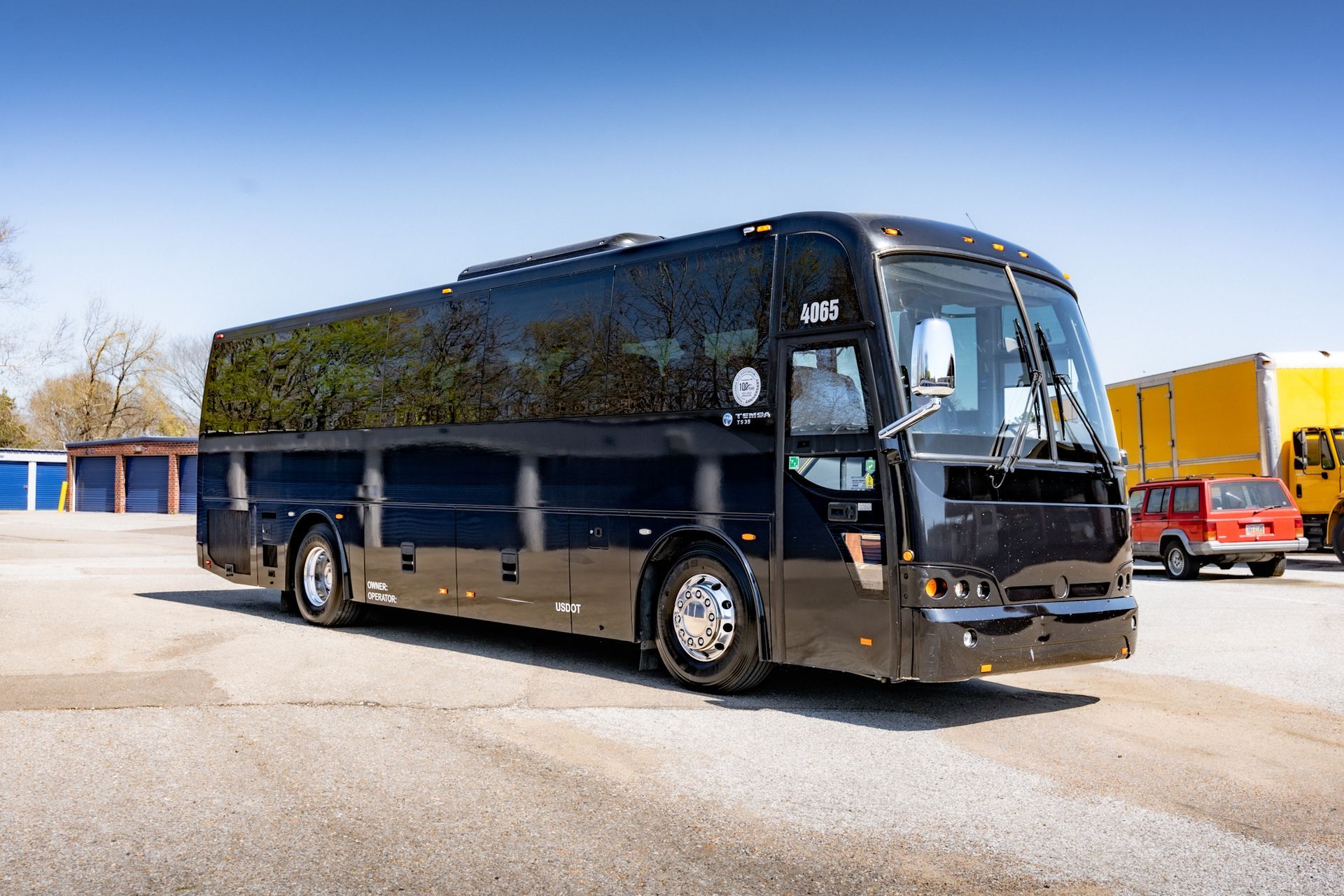 Black tour bus parked on asphalt in front of some storage units. Bright sunny day.