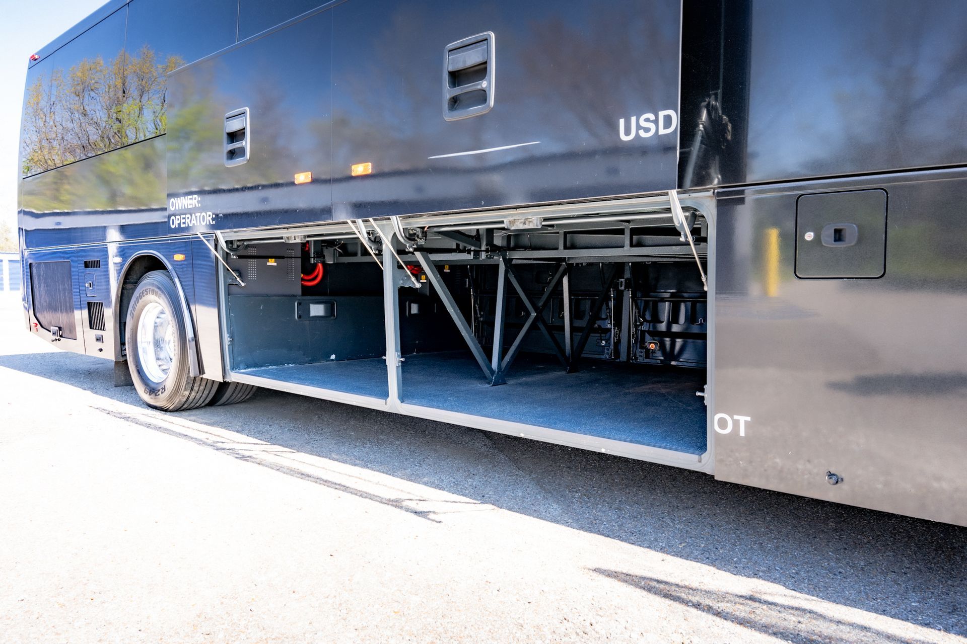 Black bus with open undercarriage compartments on asphalt.