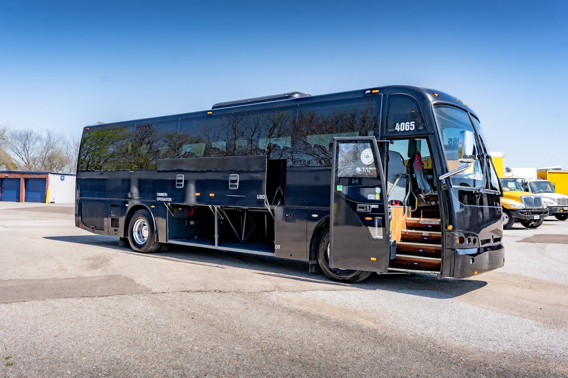 Black coach bus with open doors and luggage compartment, parked on asphalt.