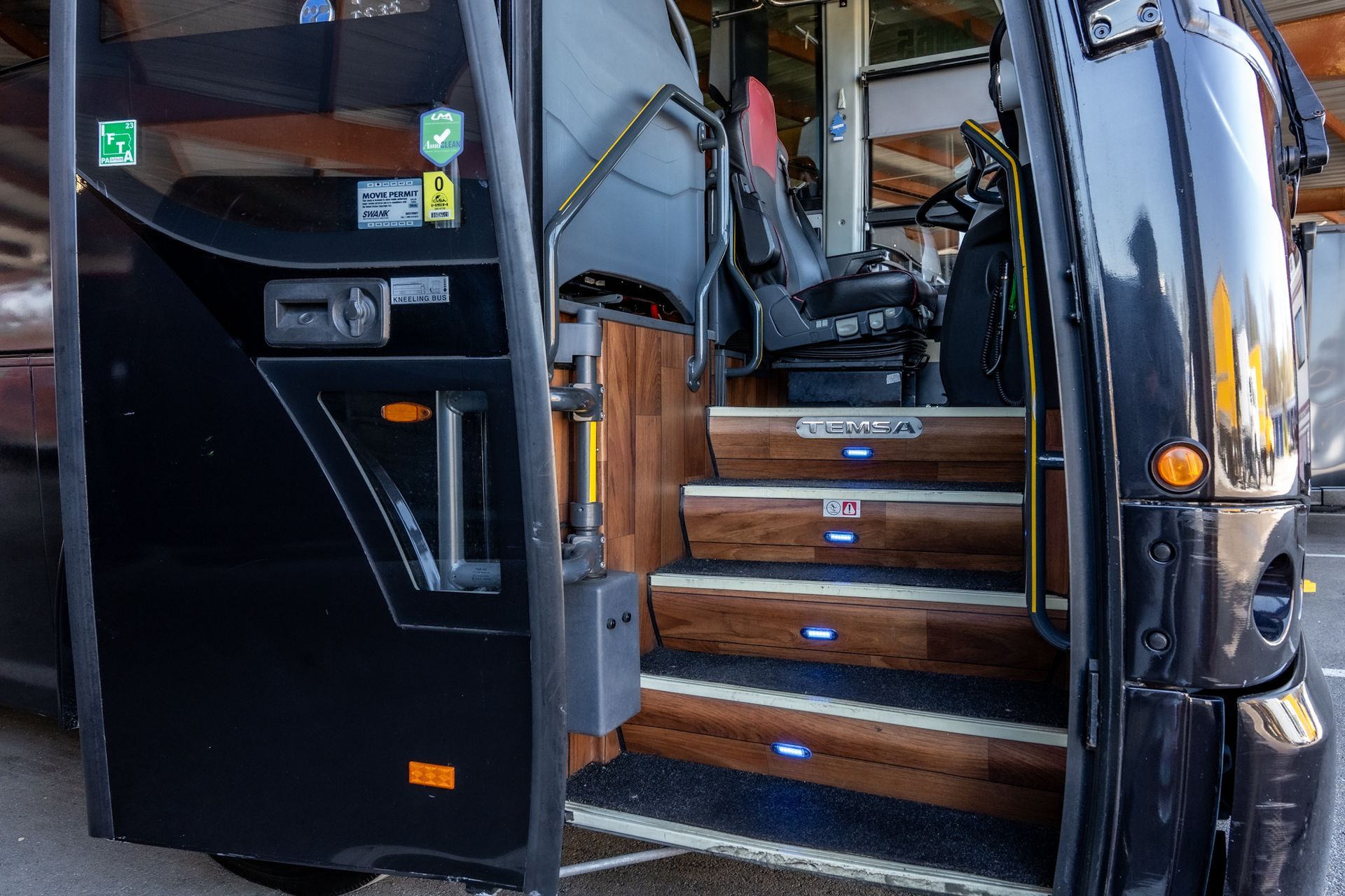 Black bus doorway with wooden steps leading inside; driver's seat visible.