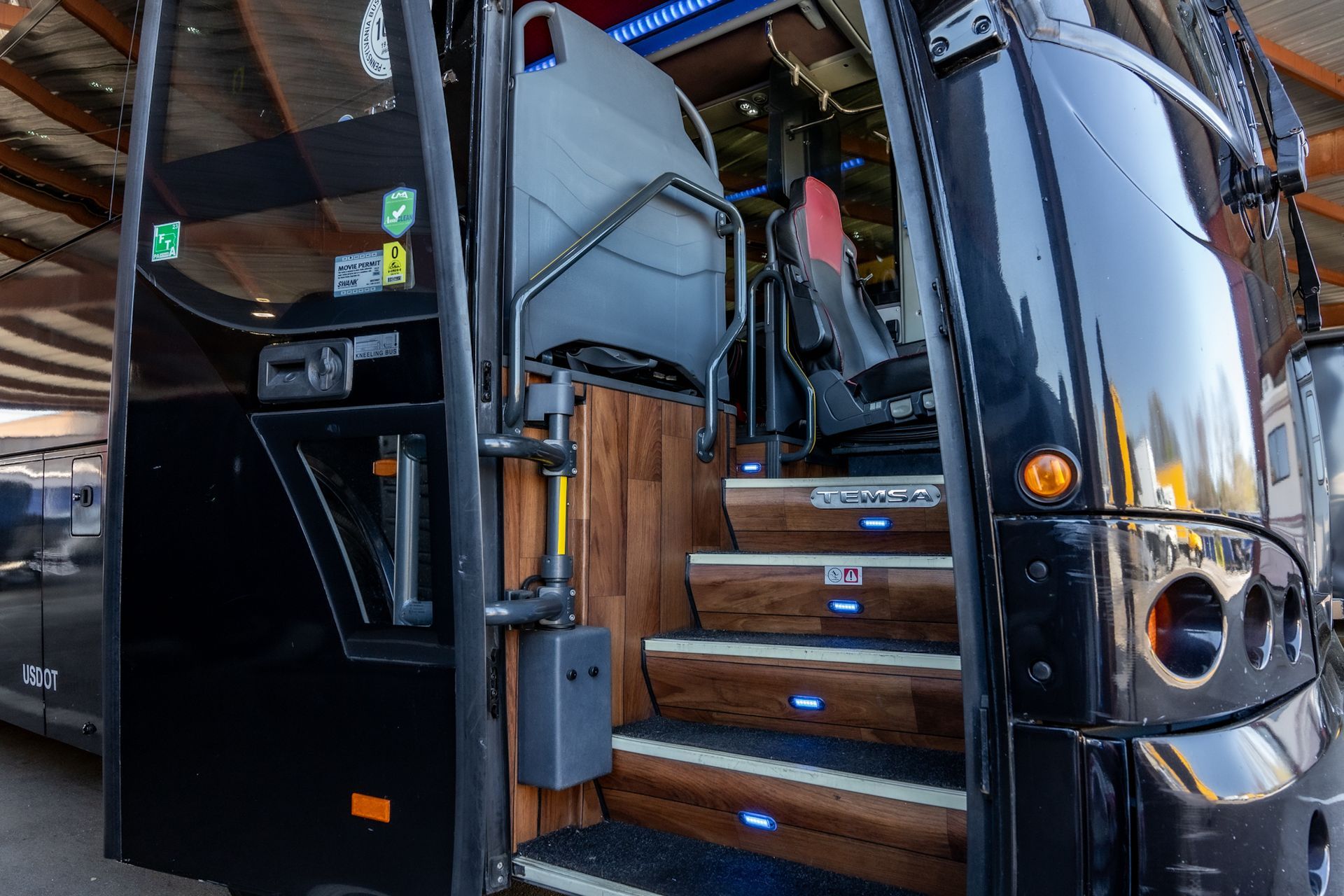 Black bus entrance with wooden stairs, metal handrail, and glowing blue step lights.