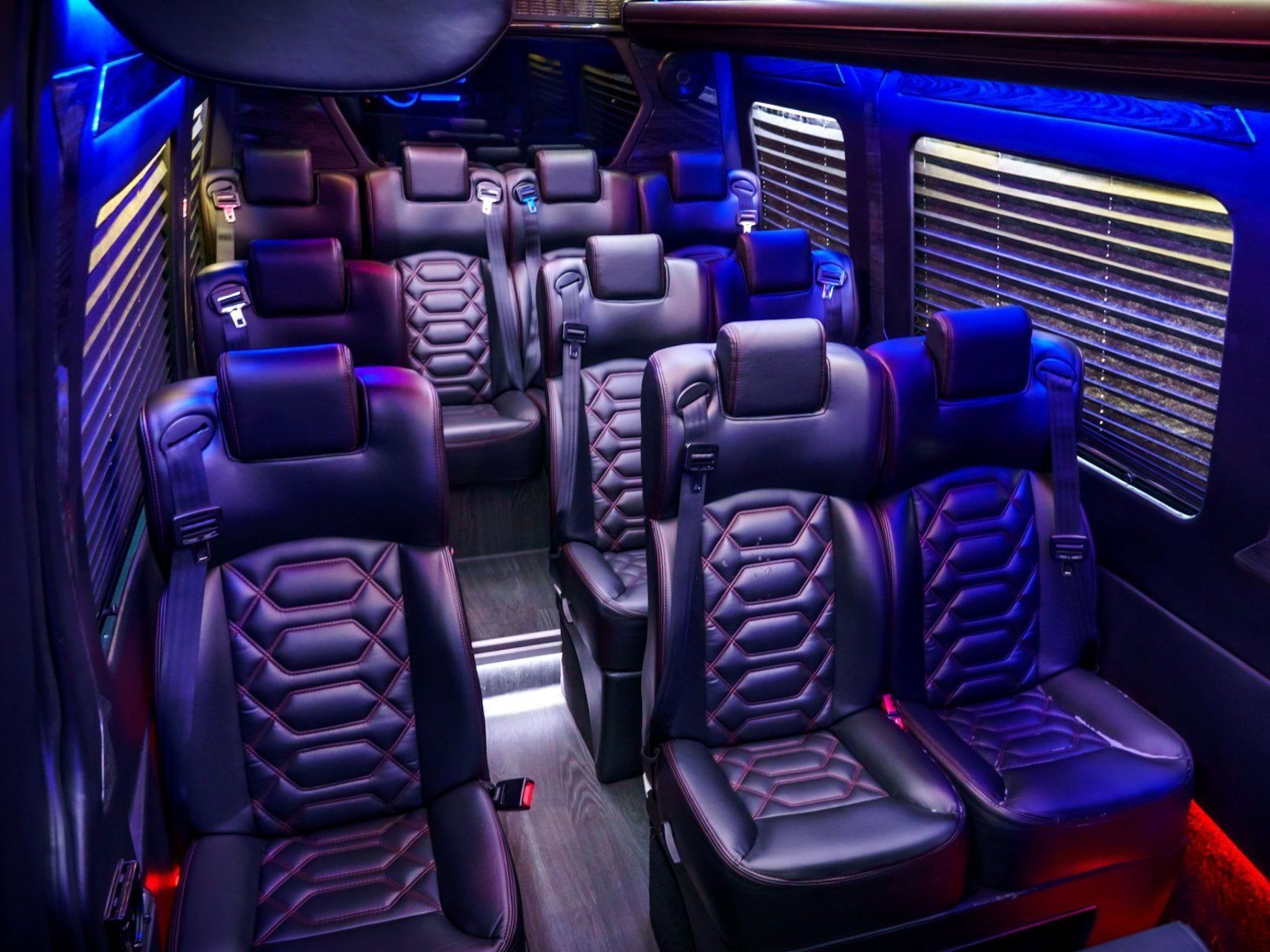 Interior of a luxury van with black leather seats, blue and green lighting, and a control panel.