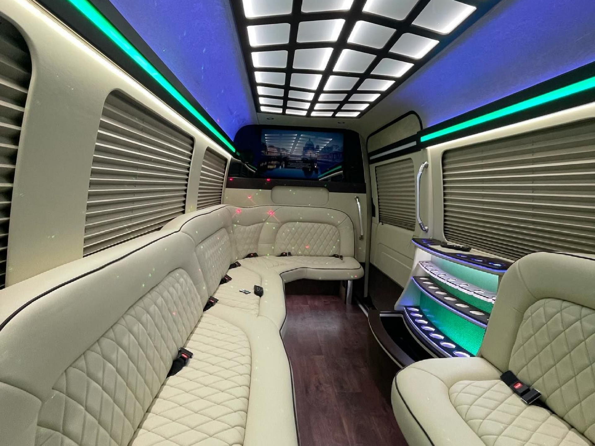 Interior of a luxury van with cream leather seating, wood floors, and LED lighting.
