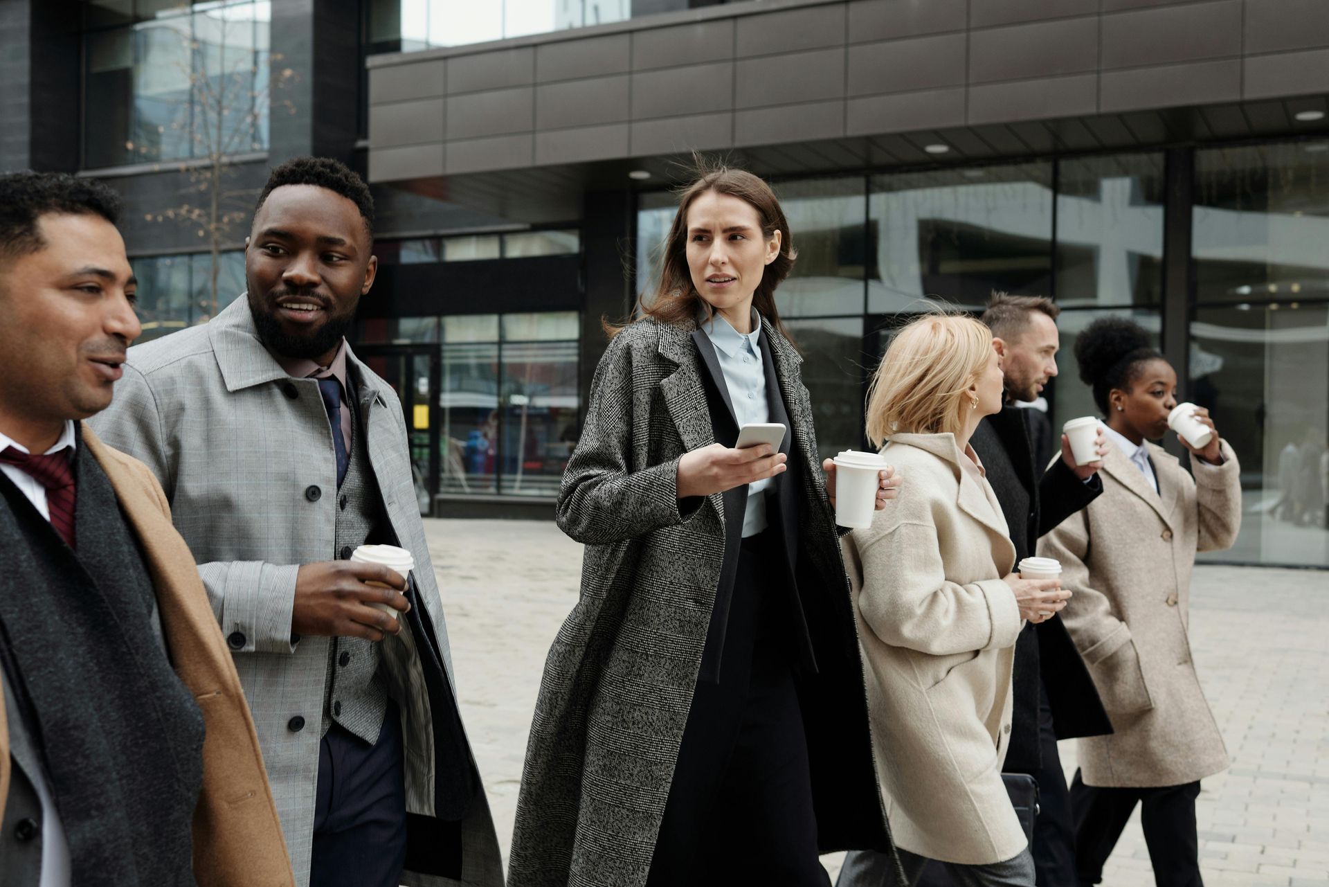 Group of professionals walking outside a modern building, holding coffee cups, and engaged in conversation.
