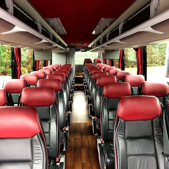Interior of a bus with red and black seats arranged in rows, wooden floors, and red ceiling.