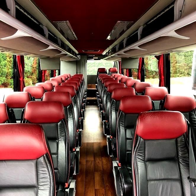Interior of a bus with rows of red and black leather seats, wooden floor, and red ceiling.