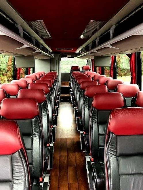 Interior of a bus, red and black seats line the aisle. Wooden floor, red ceiling.