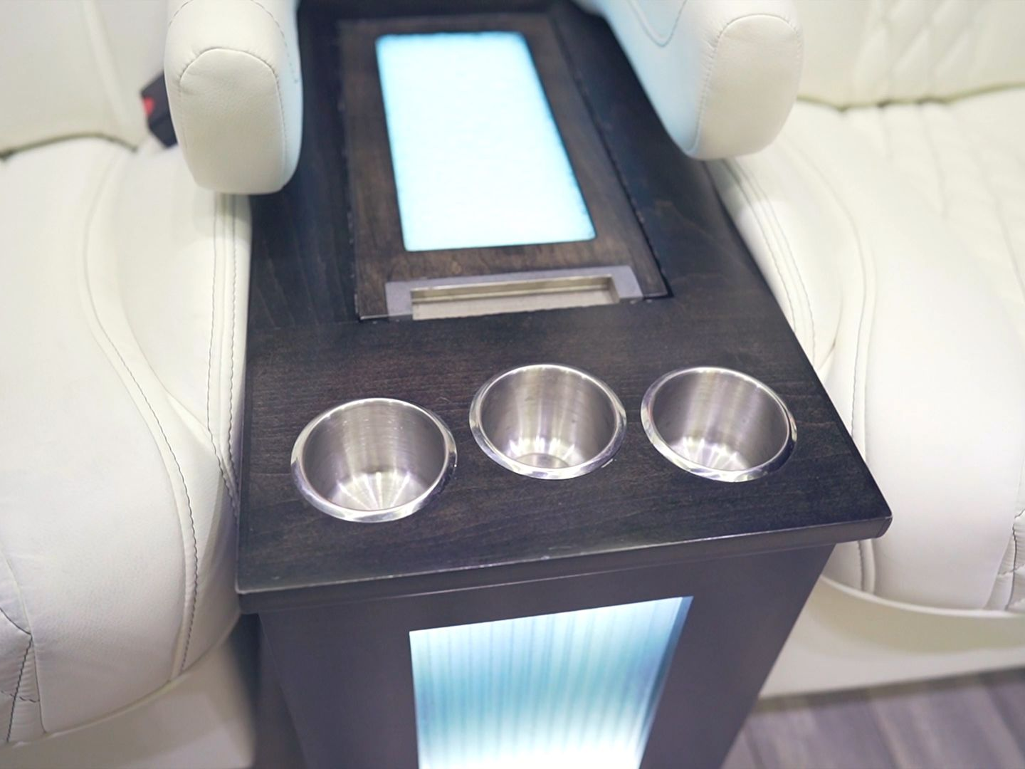 Dark wooden console with three cup holders and a glowing panel, between two white leather seats.