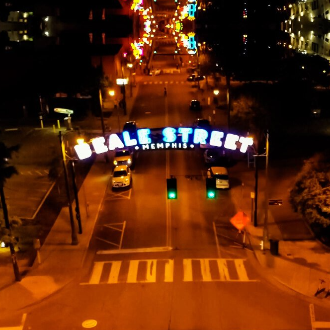 Beale Street entrance in Memphis at night, lit-up sign over street with traffic and lights.