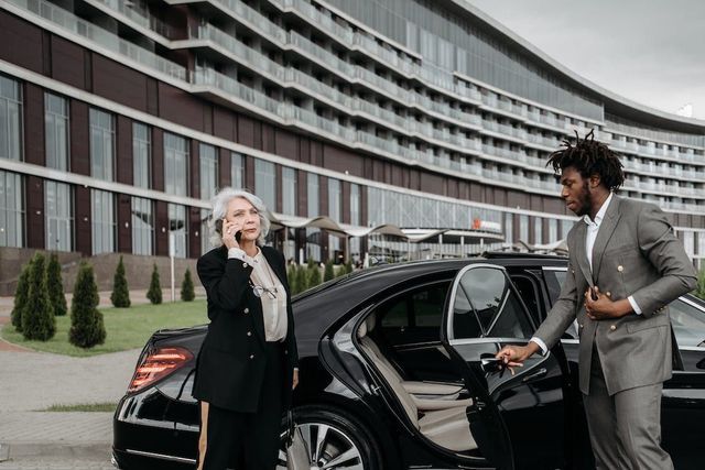 Woman on phone next to car; man in suit opening door near modern building.