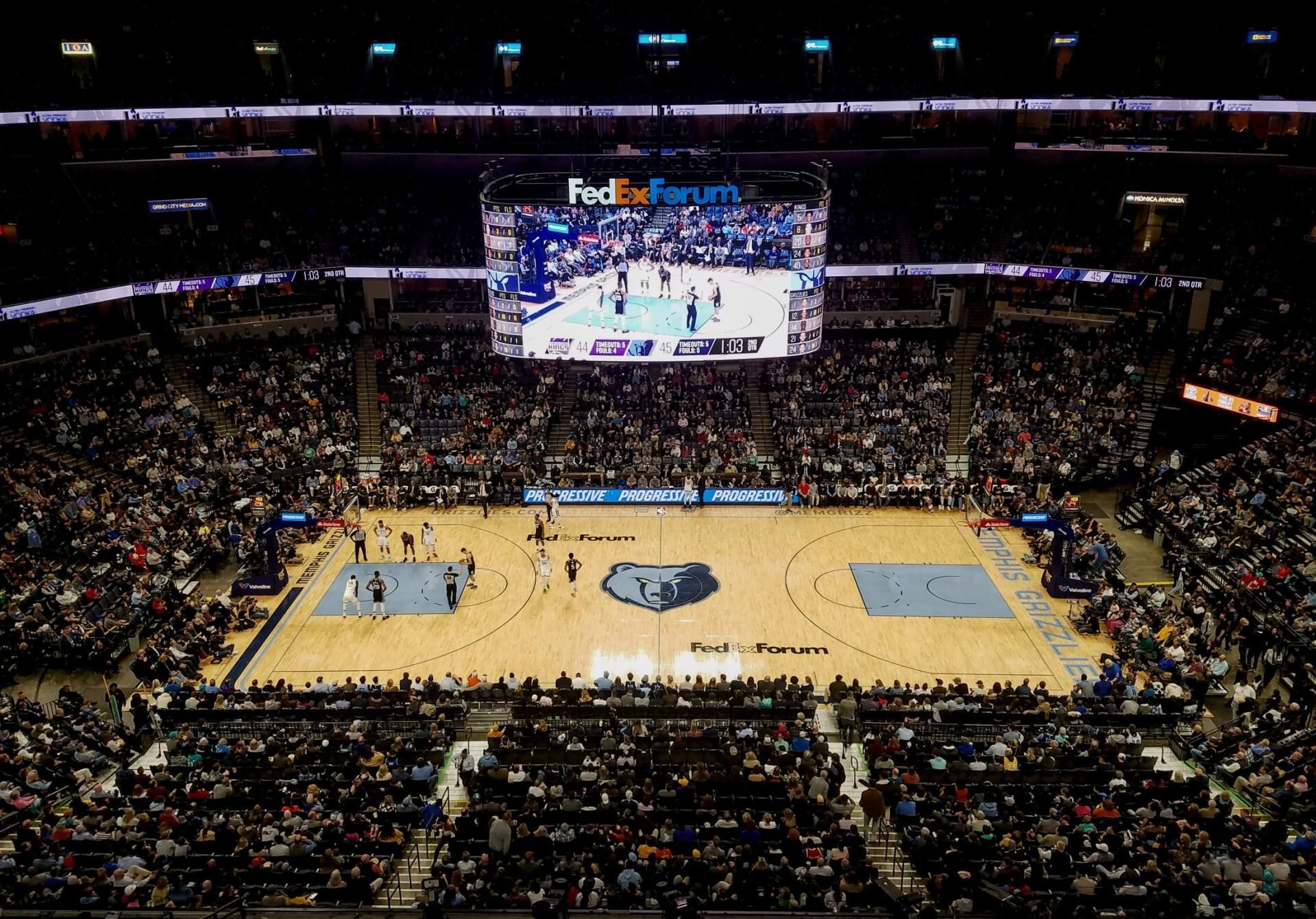 Basketball game in progress at FedExForum, Memphis. Court and crowd visible, large screen overhead. Executive coaches llc