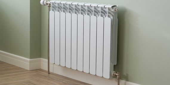 White radiator on a pale green wall above a beige carpeted floor
