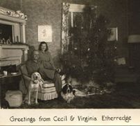 A black and white photo of a man and woman sitting in front of a christmas tree.